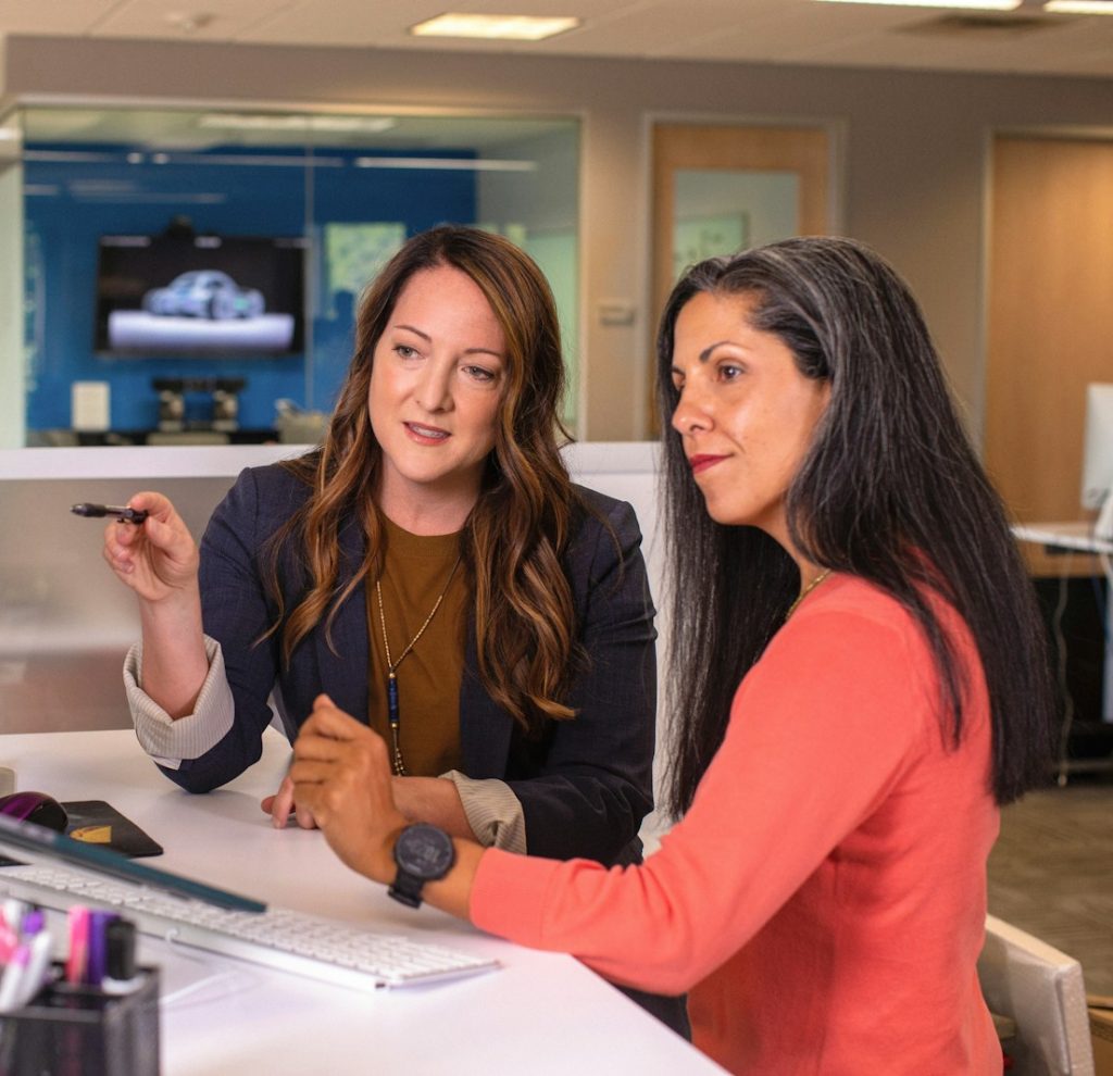 two women sitting at a table looking at a computer screen